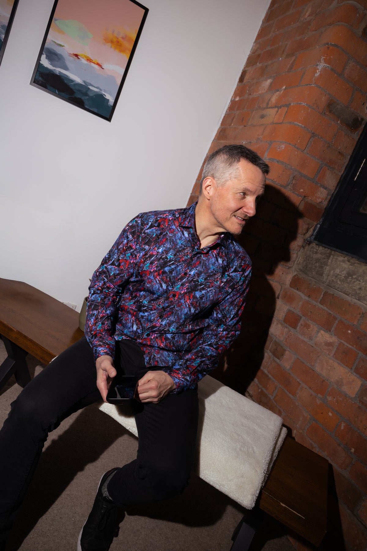 Man seated indoors wearing a blue and purple patterned shirt