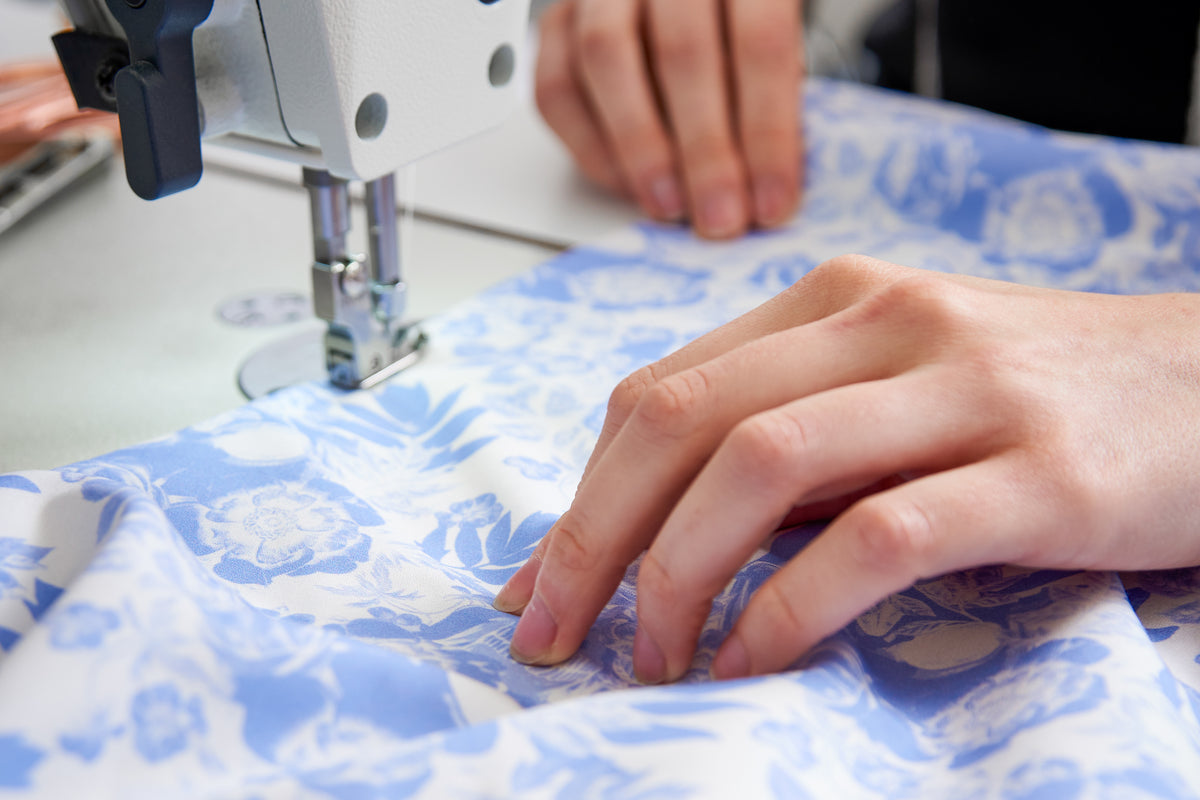 Hands guiding floral shirt fabric through a sewing machine