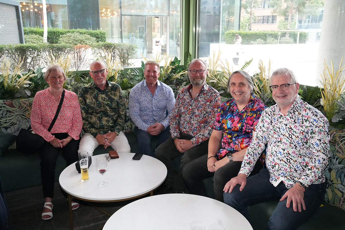Guests wearing colourful shirts gathered around a table at a Blake Mill event