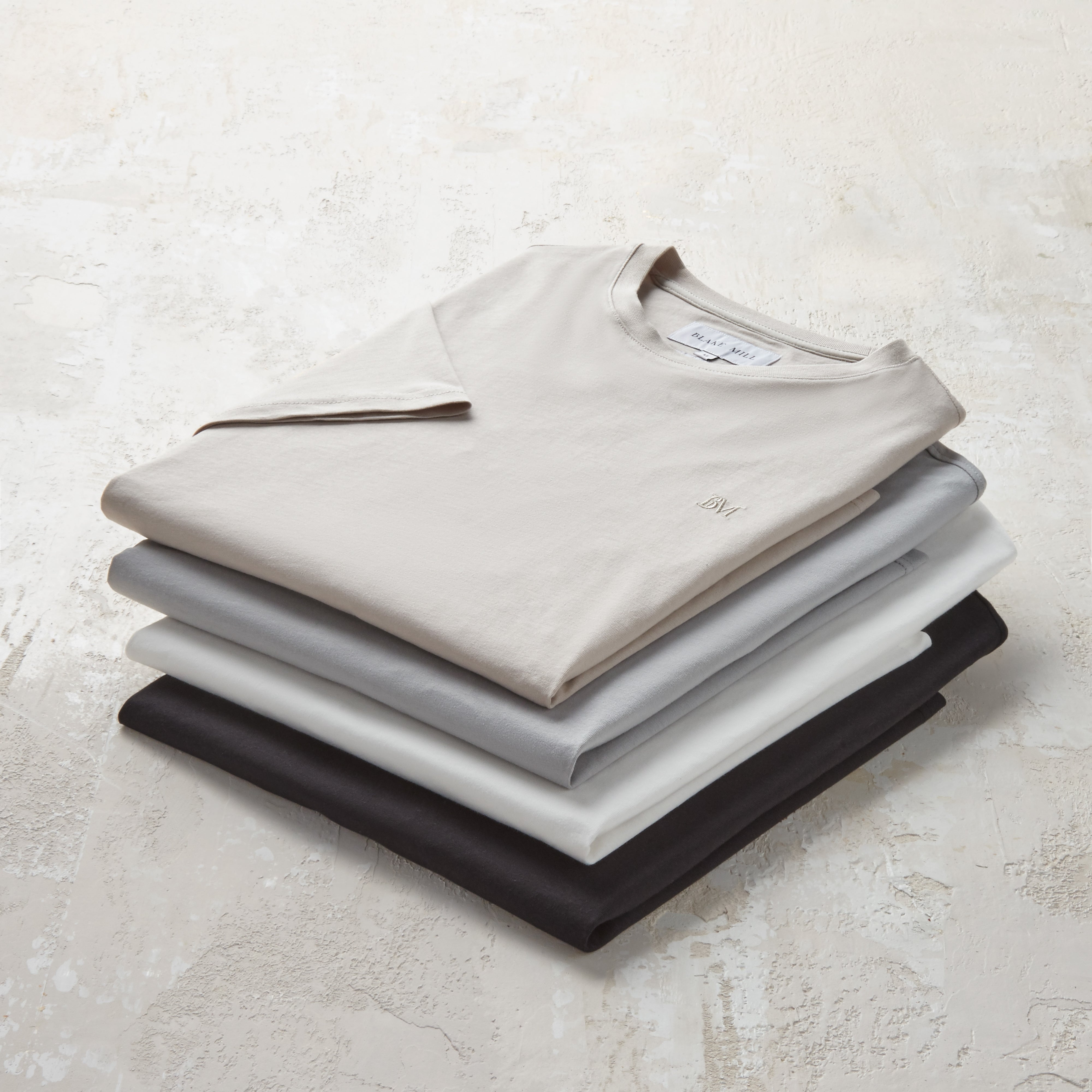 Studio image showing all four of the Blake Mill organic cotton t-shirts in a stacked pile.