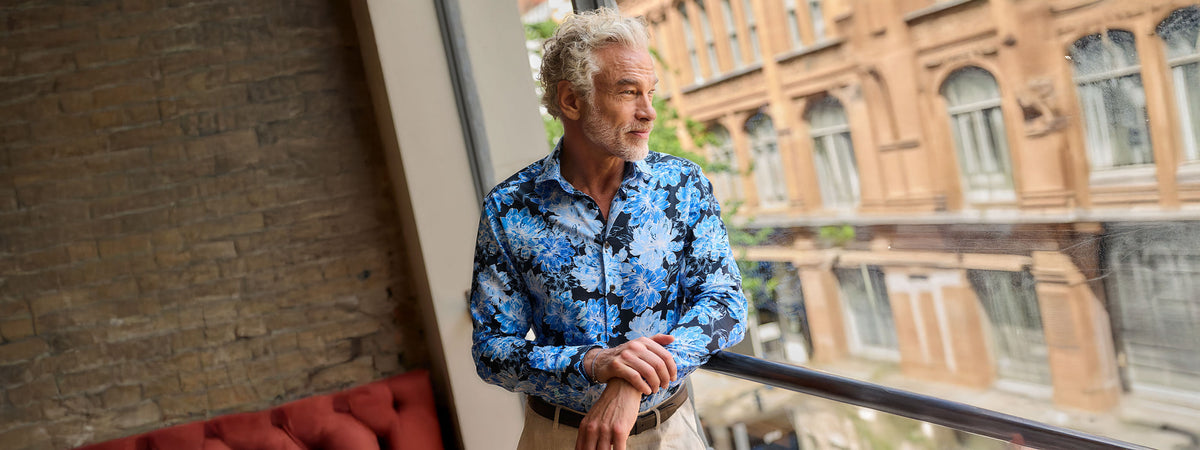 Man wearing a blue patterned shirt beside a large window
