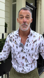 Man speaking to camera in a white shirt printed with L.S. Lowry figures